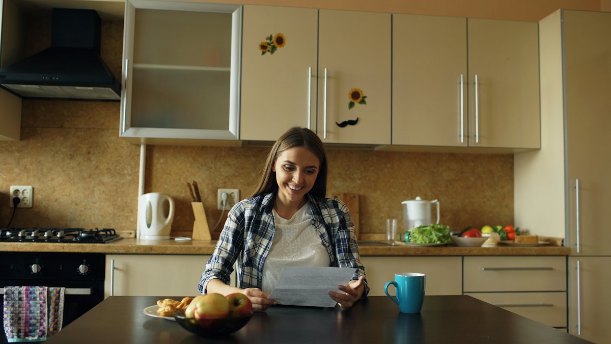 Une femme lit un courrier à la table de sa cuisine
